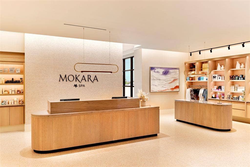 FRISCO PGA  Reception area featuring custom wood-veneer cabinetry, integrated stone-surfaced countertops, textured wall detailing, polished light-toned flooring, and minimalist linear pendant lighting