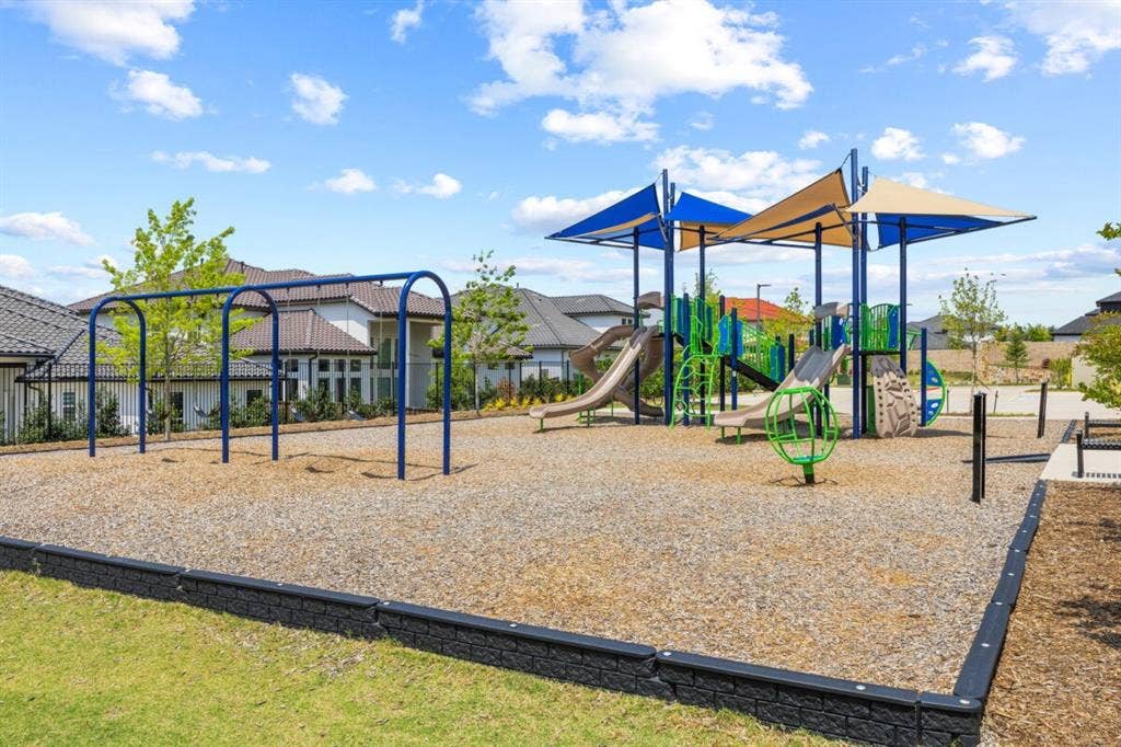 LEXINGTON Community playground featuring a multi-level structure with slides, integrated shade canopies, and a separate swing set, all contained within a bordered gravel surface