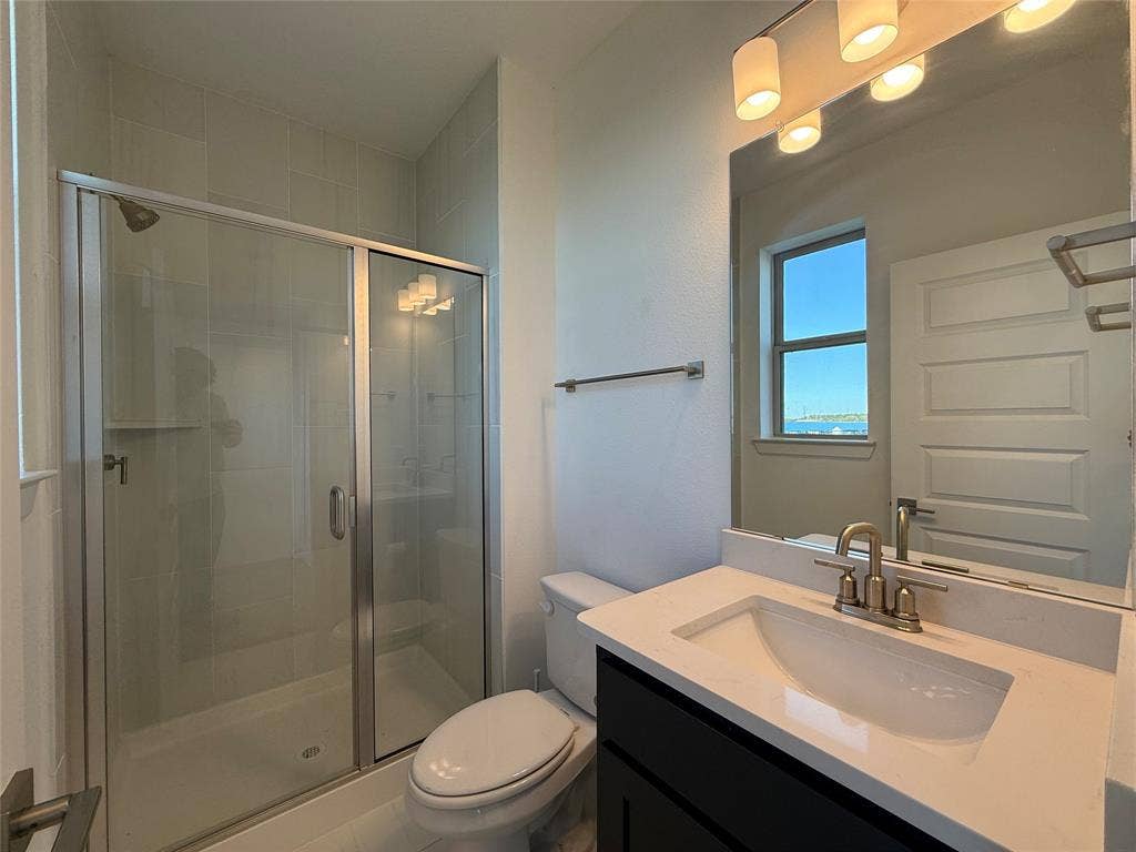 9223 Easy Street, Rowlett, TX 75088 Bathroom featuring a single-sink vanity with a solid-surface countertop, dark cabinetry, a glass-enclosed shower with tiled walls, and polished metal hardware