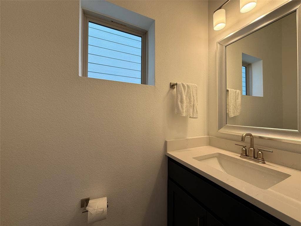 9223 Easy Street, Rowlett, TX 75088 Dark finish vanity cabinet with a white countertop and integrated basin, chrome faucet, framed mirror, and dual-light wall fixture