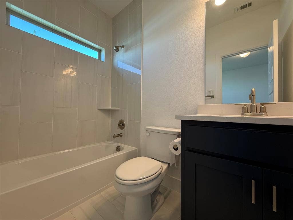 9223 Easy Street, Rowlett, TX 75088 Bathroom featuring a dark wood-finish vanity with a stone countertop, an undermount sink, a bathtub with full-height tile surround, and a horizontal clerestory window