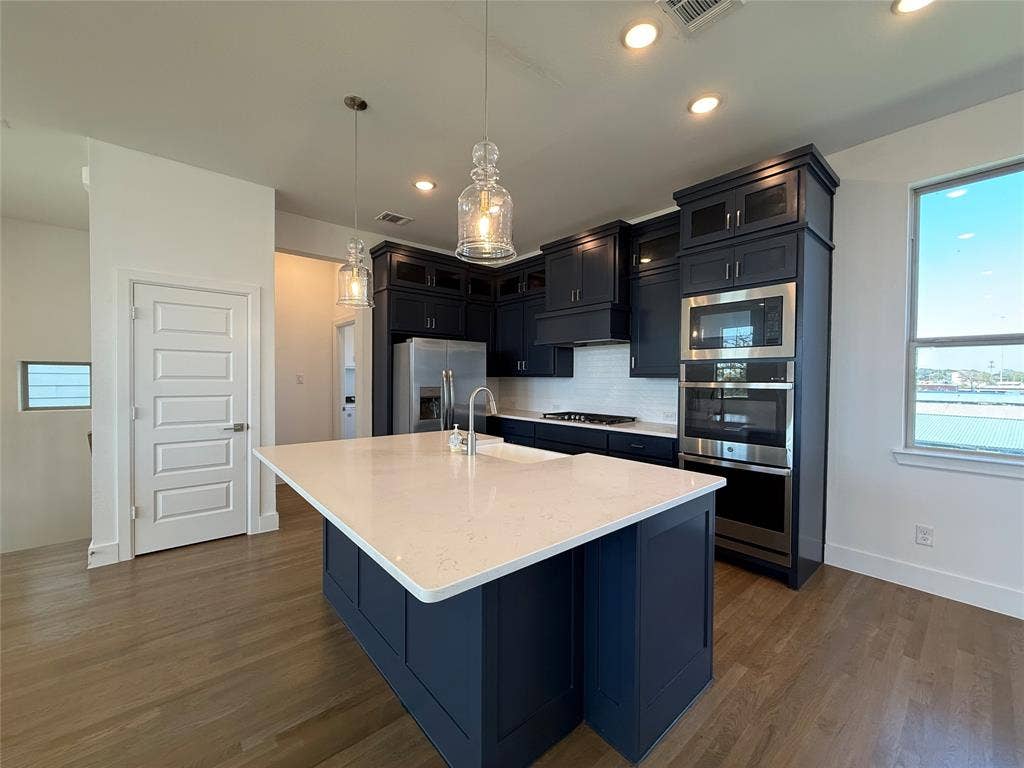 9223 Easy Street, Rowlett, TX 75088 Kitchen featuring a central island with stone countertop, dark cabinetry, stainless steel double wall oven, and wood-finish flooring