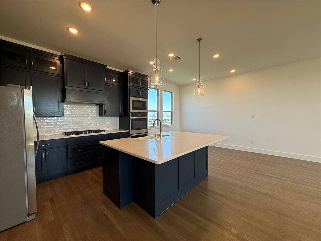 9223 Easy Street, Rowlett, TX 75088 Kitchen featuring dark cabinetry, quartz-topped island, light-colored tile backsplash, wood-finish flooring, and pendant lighting