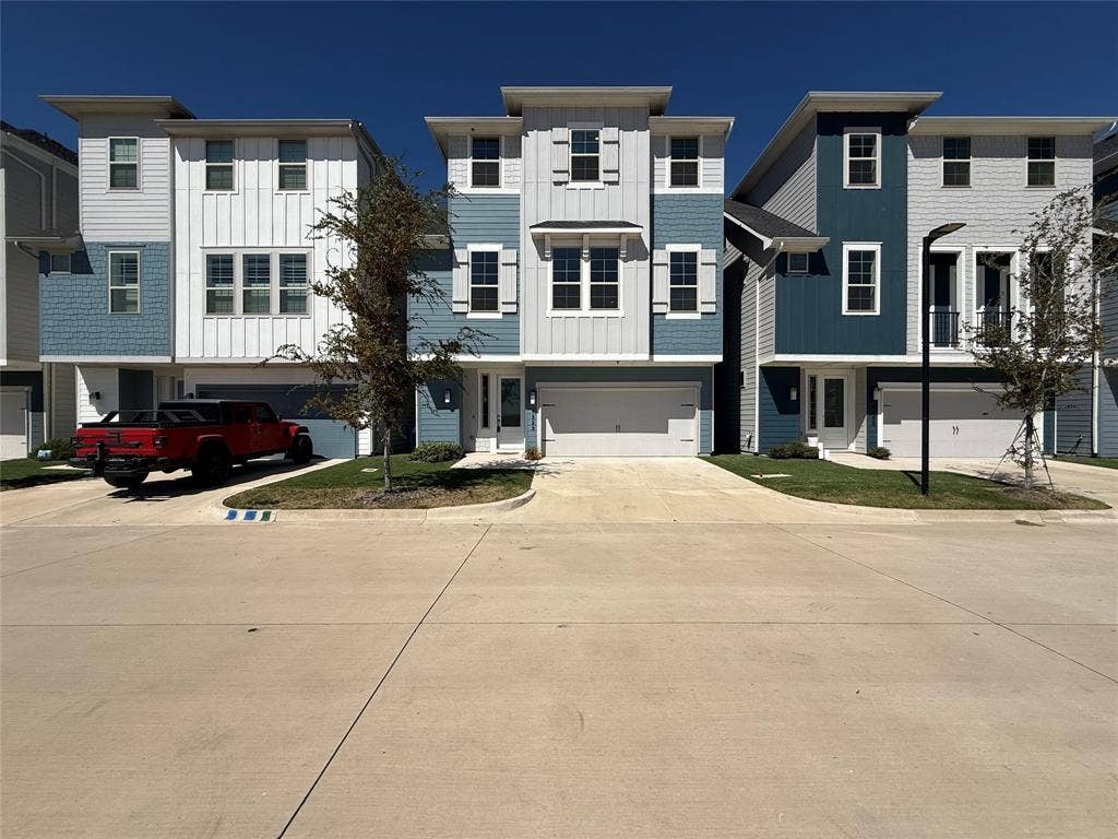 9223 Easy Street, Rowlett, TX 75088 Three-story multi-family residence featuring a mixed-material facade of vertical board-and-batten and horizontal lap siding, attached two-car garage, and shuttered windows