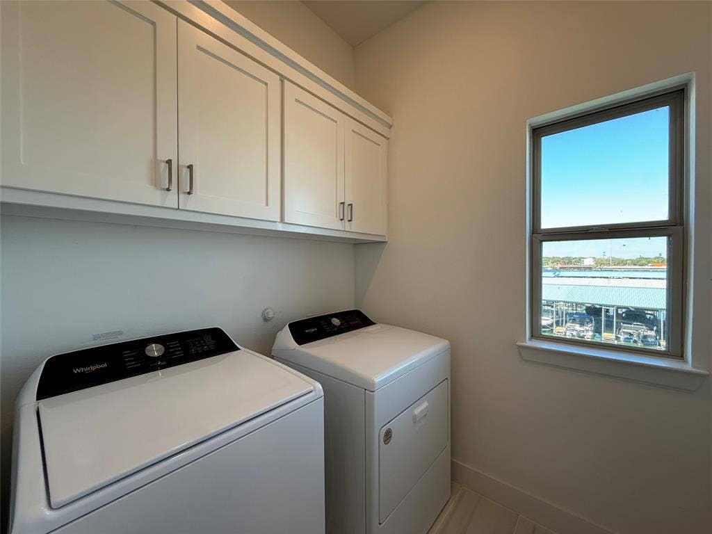 9223 Easy Street, Rowlett, TX 75088 Laundry area featuring white shaker-style wall-mounted cabinetry, integrated laundry appliances, and a window with exterior water and boat slip scenery