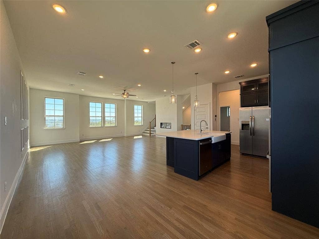 9223 Easy Street, Rowlett, TX 75088 Open-concept kitchen featuring an island with a white countertop and farmhouse sink, wood-finish flooring, recessed lighting, and stainless steel appliances