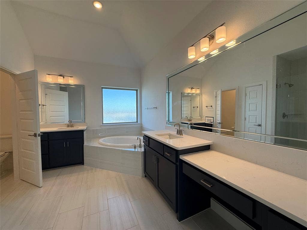 9223 Easy Street, Rowlett, TX 75088 Bathroom featuring dual dark cabinetry, white countertops, a deep soaking tub, tile flooring, and large wall-mounted mirrors