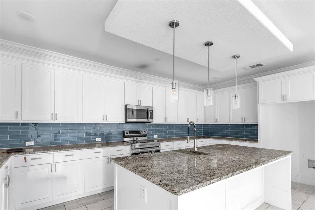 2002 Clay Street, Mabank, TX 75147 White kitchen with granite-look island, blue glass tile backsplash and stainless appliances
