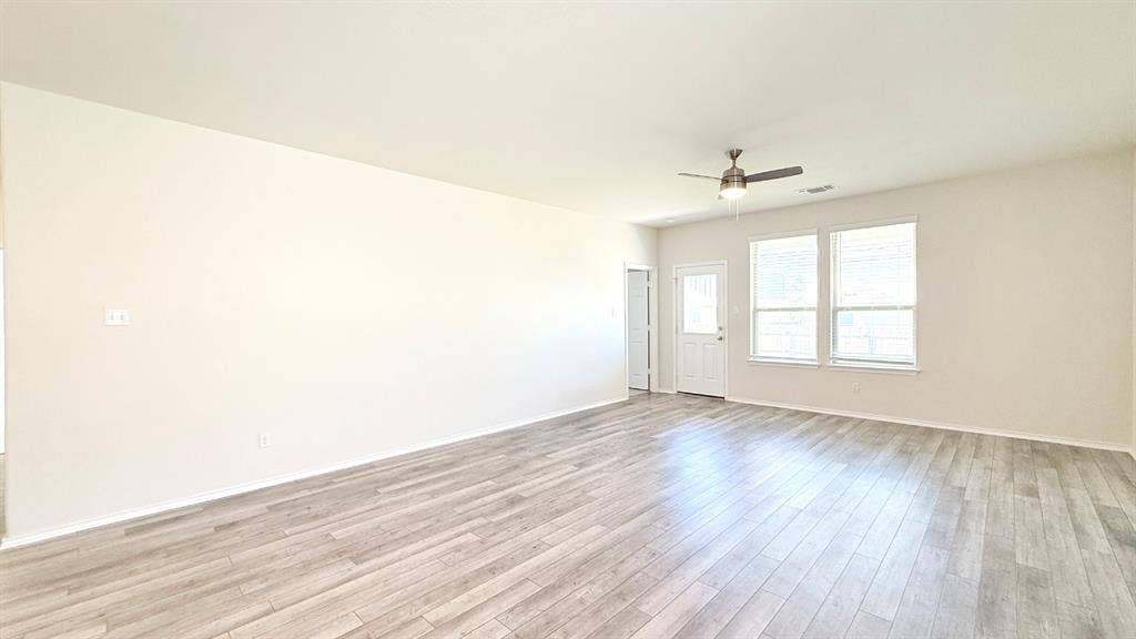 113 Onna Street, Taylor, TX 76574 Interior space featuring wood-finish flooring, neutral wall paint, two dual-pane windows, and a ceiling fan with integrated lighting