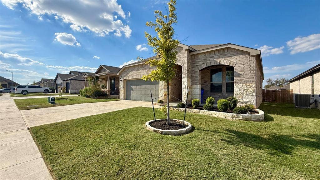 113 Onna Street, Taylor, TX 76574 Single-story residence featuring a mixed stone and brick facade, arched entryway, attached two-car garage, and a manicured front lawn with stone-bordered landscaping