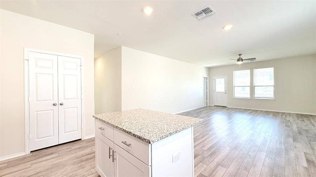 113 Onna Street, Taylor, TX 76574 Kitchen island with speckled stone countertop and white cabinetry, wood-finish flooring, recessed lighting, and a ceiling fan with integrated light fixture