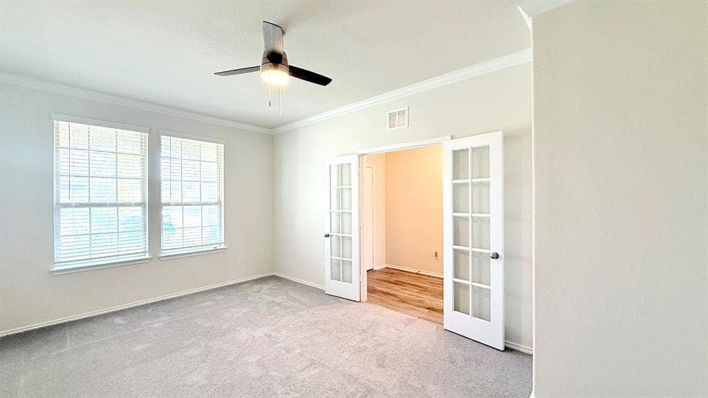 113 Onna Street, Taylor, TX 76574 Room interior featuring neutral wall paint, crown molding, a ceiling fan with integrated lighting, dual windows with blinds, and white-framed French doors with glass panes