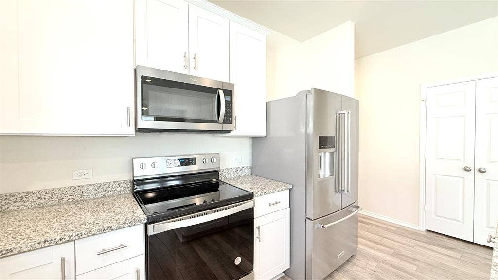 113 Onna Street, Taylor, TX 76574 Kitchen featuring white shaker-style cabinetry, speckled stone-finish countertops, stainless steel appliances, and wood-finish flooring