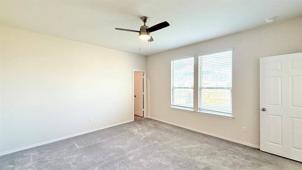 113 Onna Street, Taylor, TX 76574 Neutral-toned room featuring plush wall-to-wall carpeting, a multi-blade ceiling fan with integrated lighting, dual windows with horizontal blinds, and a six-panel door