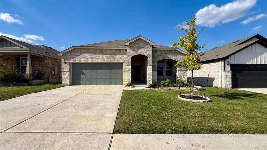 113 Onna Street, Taylor, TX 76574 Stone facade exterior featuring a covered entryway, arched window detailing, two-car garage, and a landscaped front yard with a concrete driveway