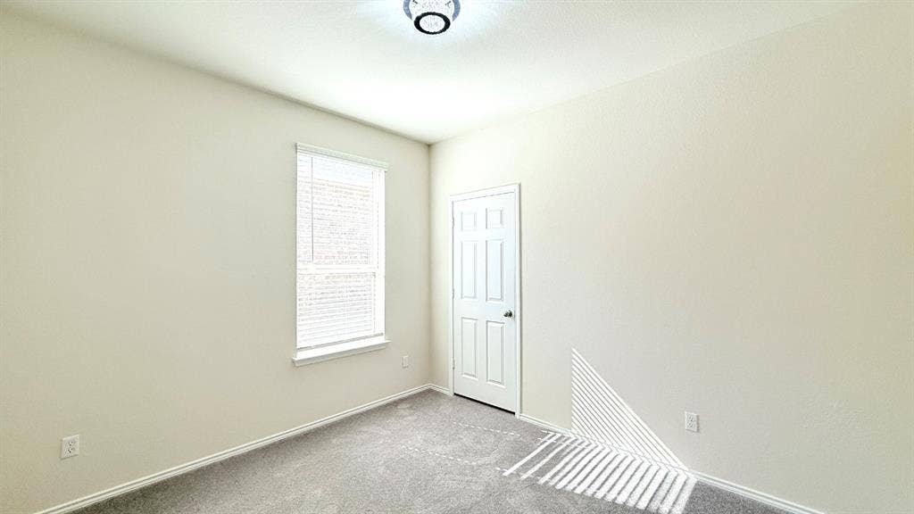 113 Onna Street, Taylor, TX 76574 Interior room featuring neutral-toned carpeting, a six-panel door, a single-pane window with integrated blinds, and a circular flush-mount ceiling fixture