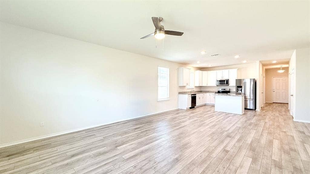 113 Onna Street, Taylor, TX 76574 Open-concept interior featuring wood-finish flooring, white cabinetry, stone-finish countertops, stainless steel appliances, and a ceiling-mounted light fixture with a fan