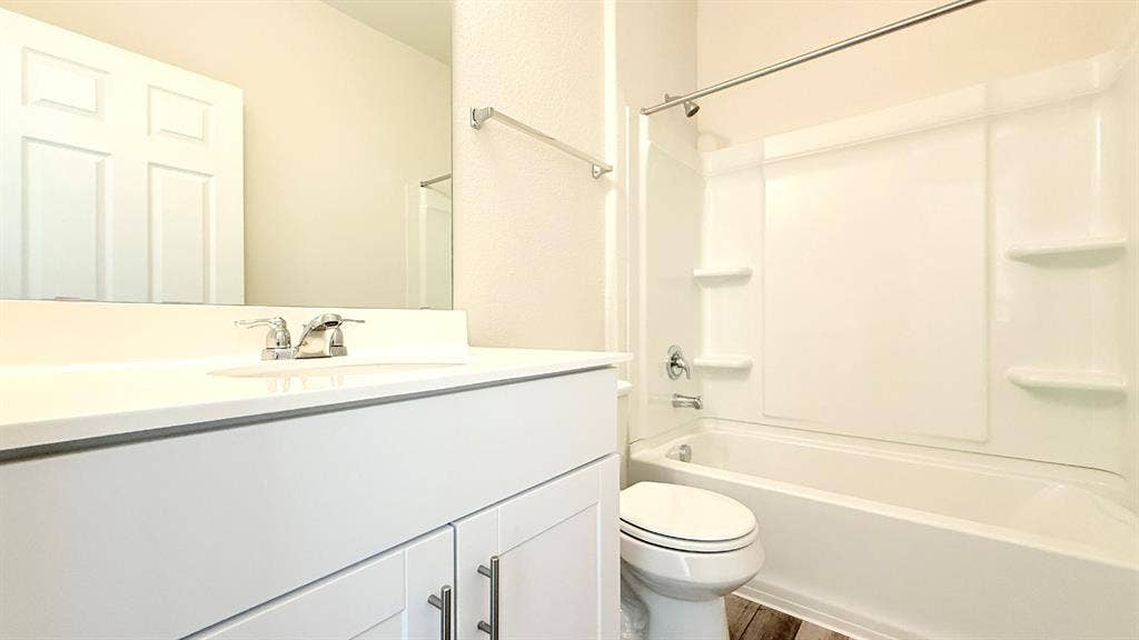 113 Onna Street, Taylor, TX 76574 Bathroom featuring a white vanity cabinet with metallic hardware, a crisp white countertop with an integrated basin, a polished chrome faucet, and a combination tub and shower surround with built-in shelving