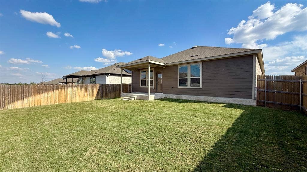 113 Onna Street, Taylor, TX 76574 Private backyard featuring a manicured lawn, covered patio, stone veneer accents, and wood-style siding
