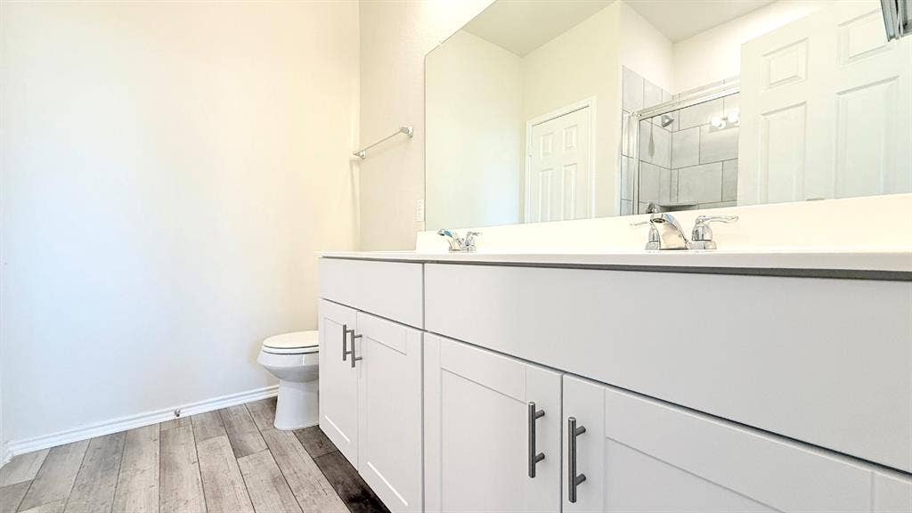 113 Onna Street, Taylor, TX 76574 White vanity cabinetry featuring brushed metal hardware, dual chrome faucets, a solid-surface countertop, and wood-finish flooring
