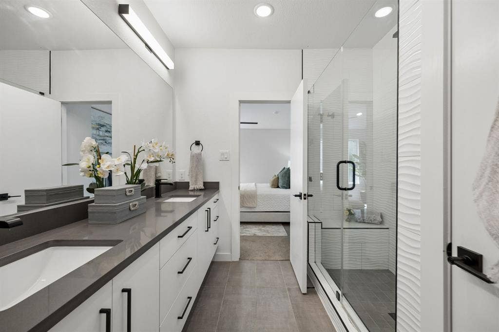 1901 N Carroll Avenue, #104, Dallas, TX 75204 Dual-sink vanity with matte black hardware, quartz countertops, full-width mirror, glass-enclosed shower with textured wall tile, and porcelain tile flooring