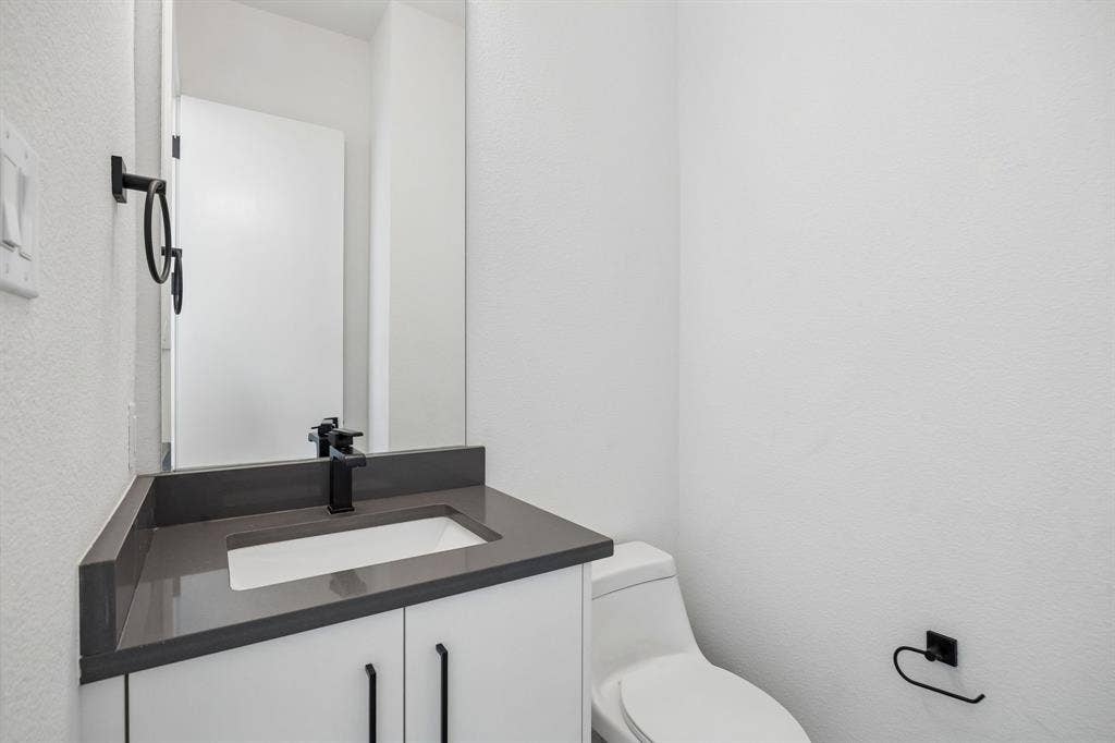 1901 N Carroll Avenue, #104, Dallas, TX 75204 Modern vanity featuring a stone-composite countertop, undermount sink, matte black faucet, and white shaker-style cabinetry with matching hardware
