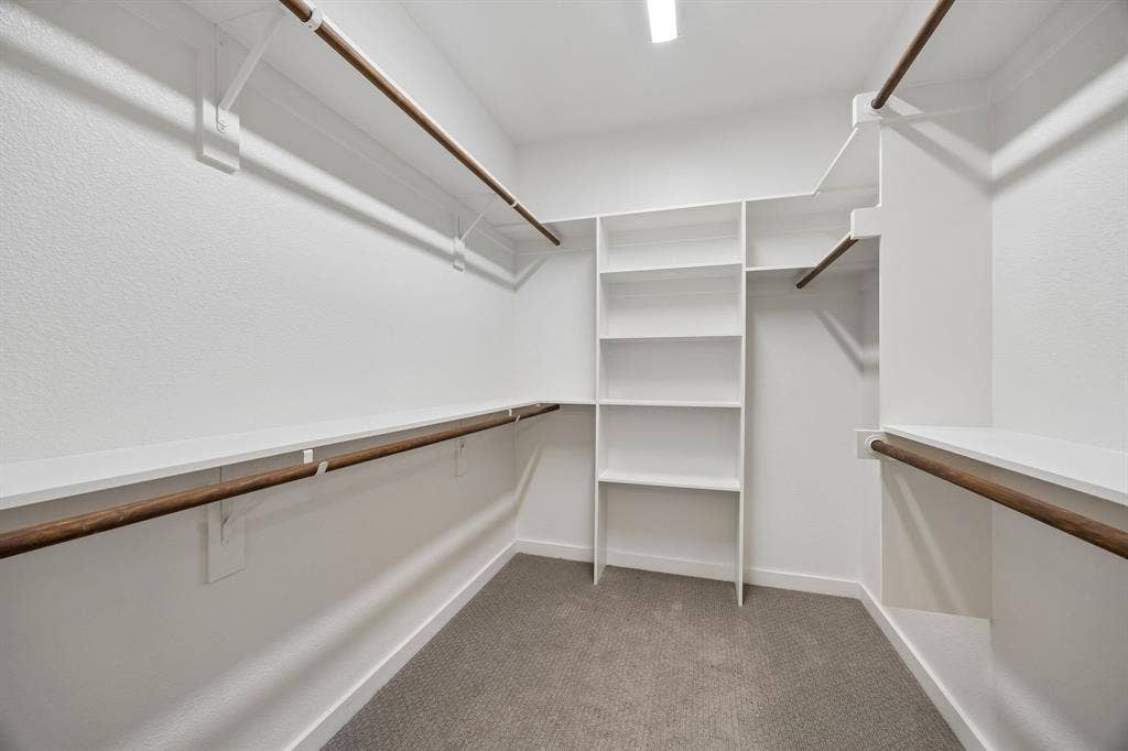 1901 N Carroll Avenue, #104, Dallas, TX 75204 Walk-in closet featuring white built-in shelving, multi-level clothing rods with wood-finish accents, and neutral carpeting