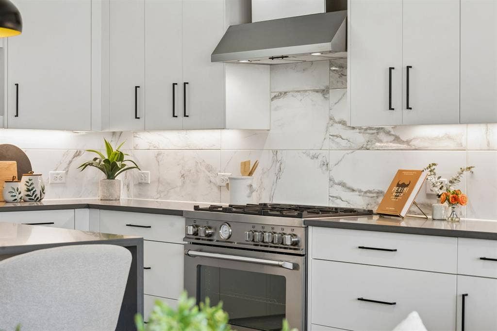 1901 N Carroll Avenue, #104, Dallas, TX 75204 Kitchen featuring flat-panel cabinetry, matte black hardware, stone-finish countertops, large-format tile backsplash, and stainless steel gas range with overhead vent hood