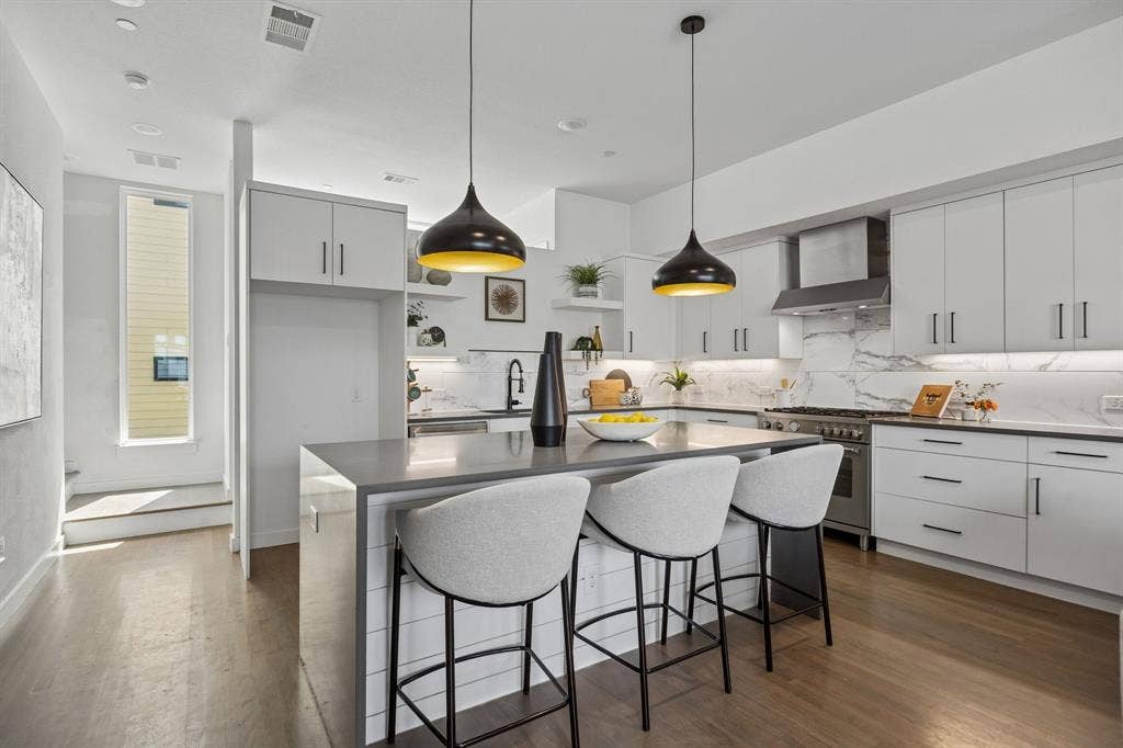 1901 N Carroll Avenue, #104, Dallas, TX 75204 Kitchen featuring white shaker-style cabinetry, quartz countertops, a stone-patterned backsplash, wood-finish flooring, and two pendant lights