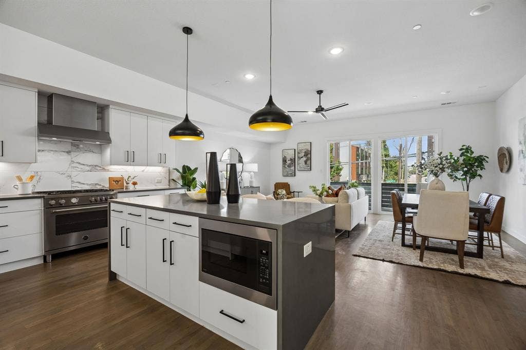 1901 N Carroll Avenue, #104, Dallas, TX 75204 Kitchen featuring a center island with solid-surface countertop, flat-panel cabinetry, professional-style stainless steel range, full-height stone-look backsplash, and dual pendant lighting