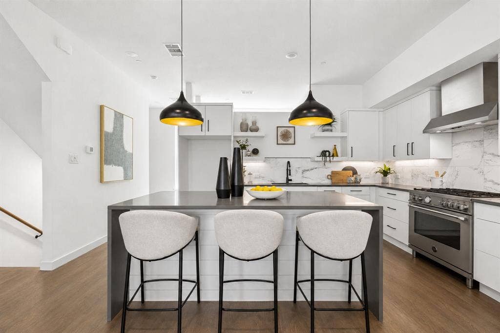 1901 N Carroll Avenue, #104, Dallas, TX 75204 Kitchen featuring a waterfall-edge center island, white cabinetry, professional-grade stainless steel range, patterned stone-finish backsplash, and wood-finish flooring