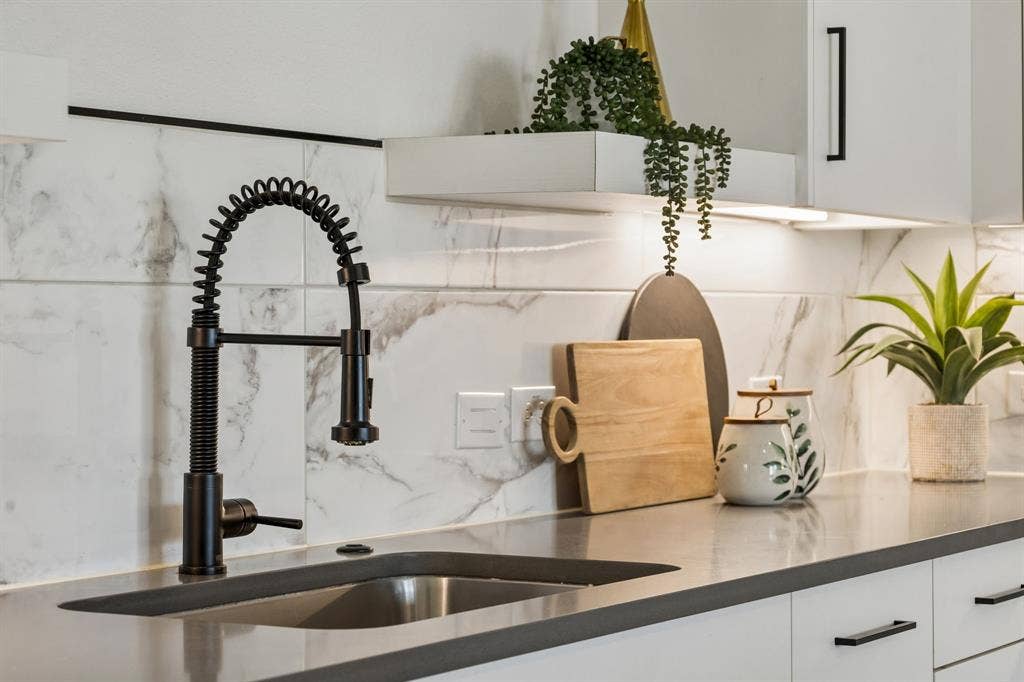 1901 N Carroll Avenue, #104, Dallas, TX 75204 Kitchen featuring a matte black industrial-style spring faucet, undermount sink, solid surface countertop, white cabinetry with matte black hardware, and large-format tile backsplash