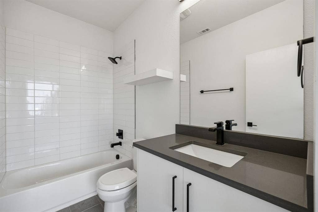 1901 N Carroll Avenue, #104, Dallas, TX 75204 Bathroom featuring a white vanity with a dark gray countertop, undermount sink, matte black hardware, and a tub-shower combination with floor-to-ceiling white tile