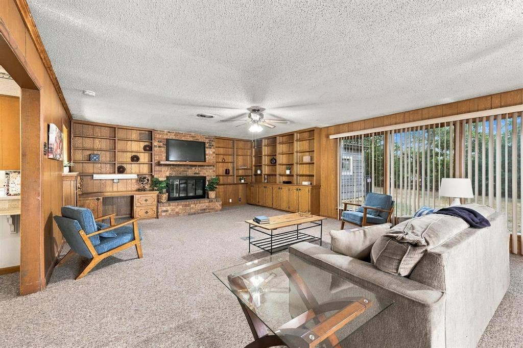 Living area featuring floor-to-ceiling wood-paneling, custom built-in cabinetry, brick-surround fireplace, and full-length sliding glass doors bringing in natural light