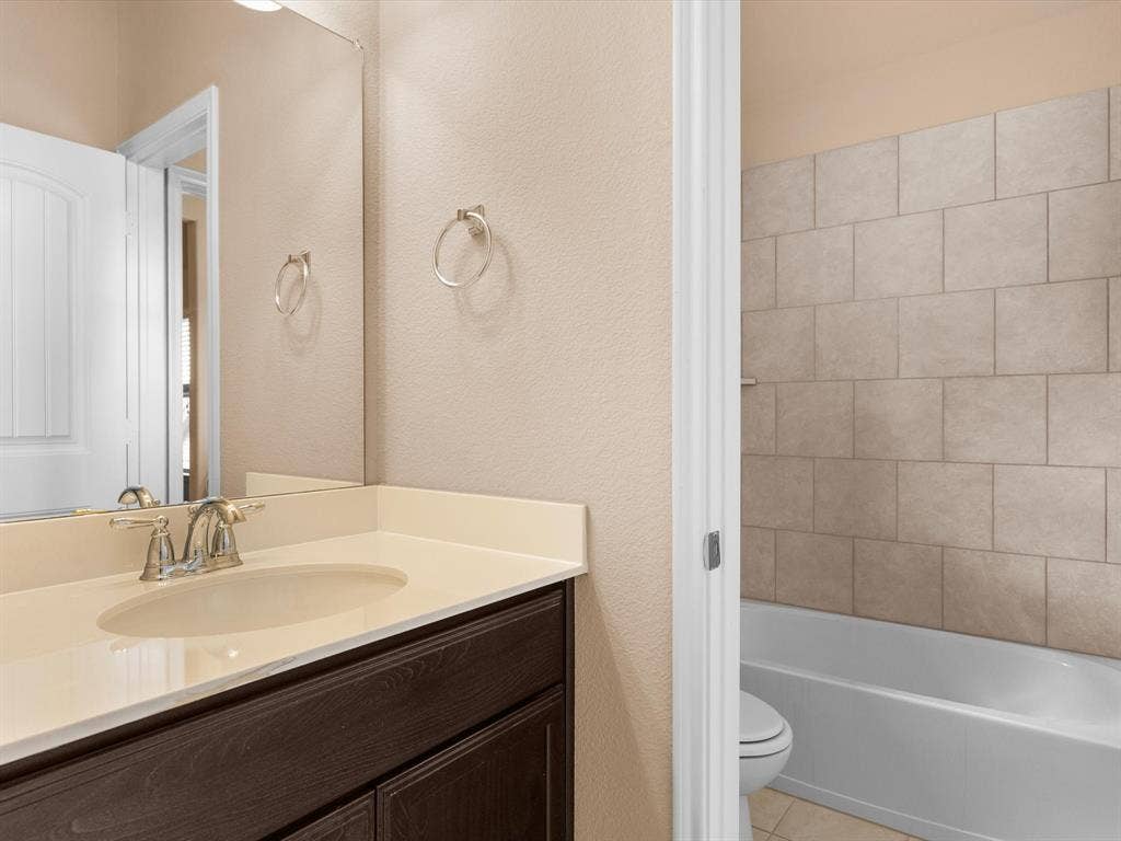 Dark wood-finish vanity with a solid surface countertop, integrated sink, large wall-mounted mirror, and a tub-shower combination with ceramic tile surround