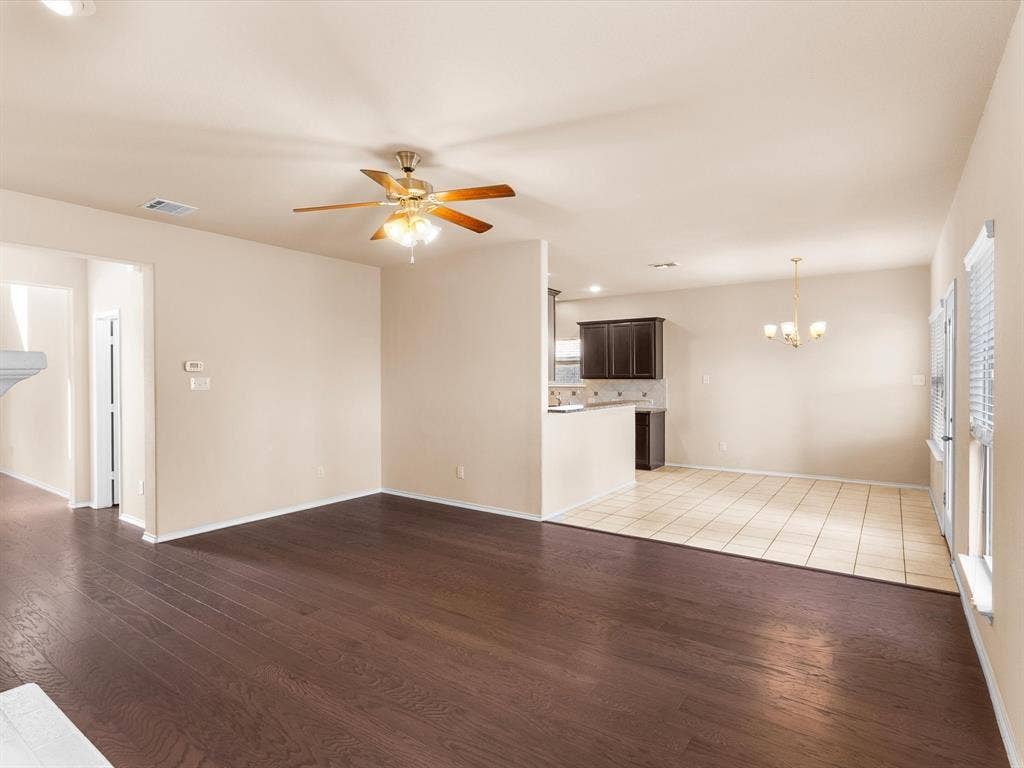 Open interior featuring wood-finish flooring, neutral wall paint, dark-toned kitchen cabinetry, tile flooring, and a ceiling fan with integrated lighting