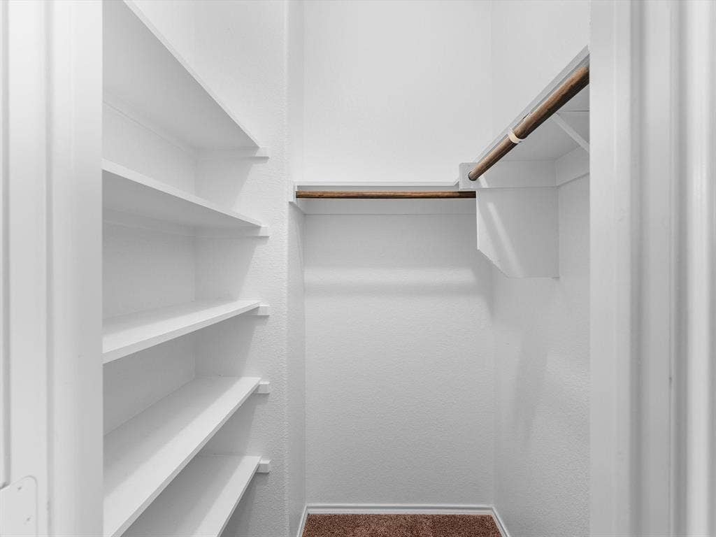 Storage space featuring white built-in shelving and a wood-finish hanging rod