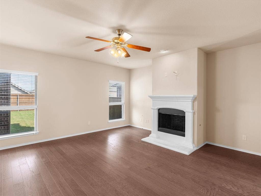 Living area featuring wood-finish flooring, white fireplace mantel with brick surround, and ceiling fan with integrated light fixture