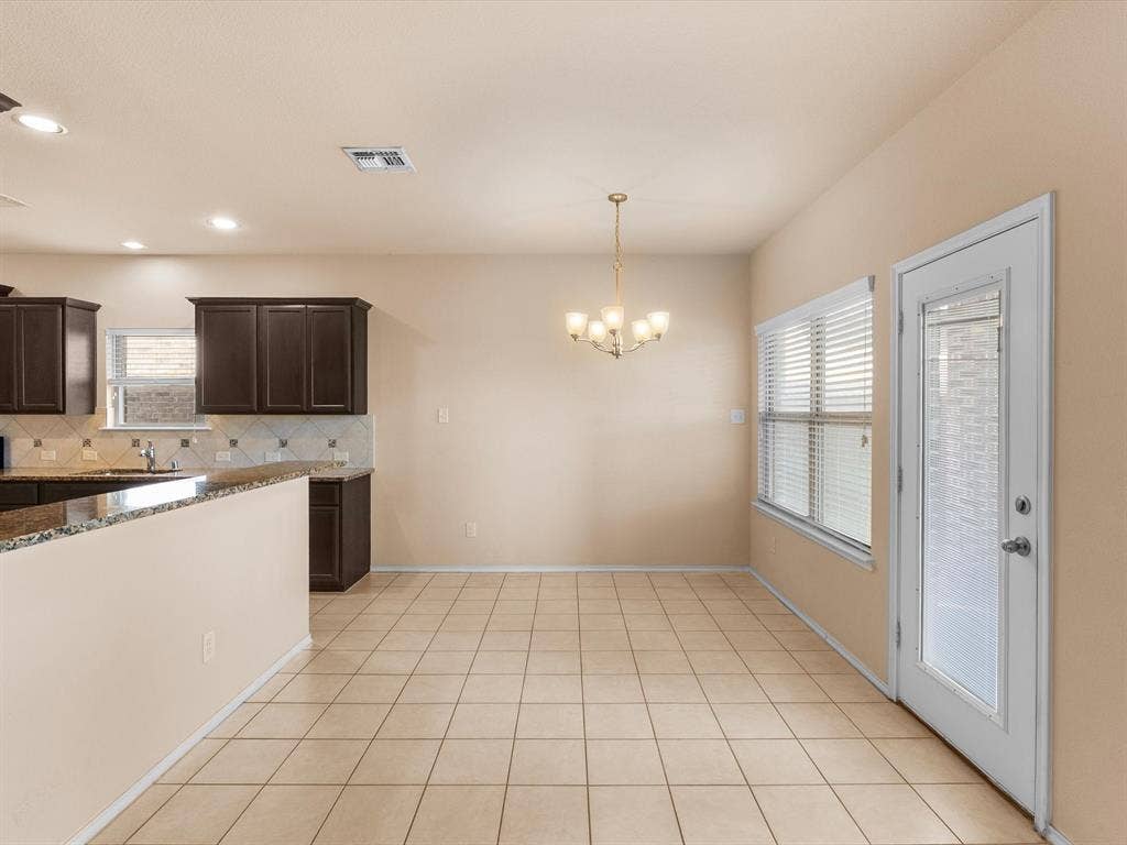 Spacious area featuring tile flooring, stone-surfaced peninsula, dark wood-finish cabinetry, multi-light chandelier, and full-glass door