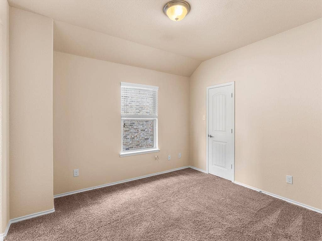 Neutral wall tones, plush carpeted flooring, vaulted ceiling, single-panel interior door, and a recessed window