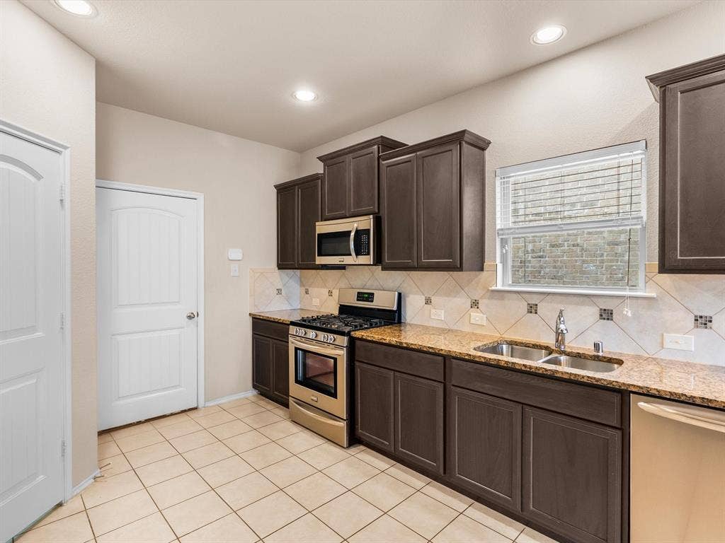 Kitchen featuring dark-finish cabinetry, stone-surface countertops, stainless steel appliances, ceramic tile backsplash with decorative accents, and tiled flooring