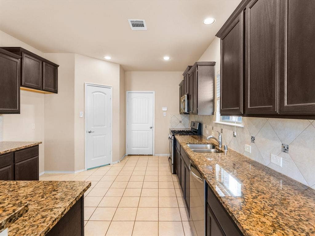 Kitchen featuring dark wood cabinetry, stone countertops, diagonal tile backsplash, ceramic tile flooring, and stainless steel appliances