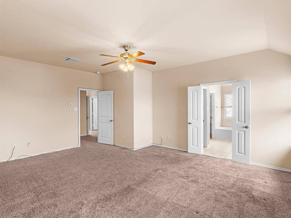 Spacious room featuring vaulted ceilings, neutral wall tones, wall-to-wall carpeting, a multi-blade ceiling fan with integrated lighting, and white six-panel interior doors