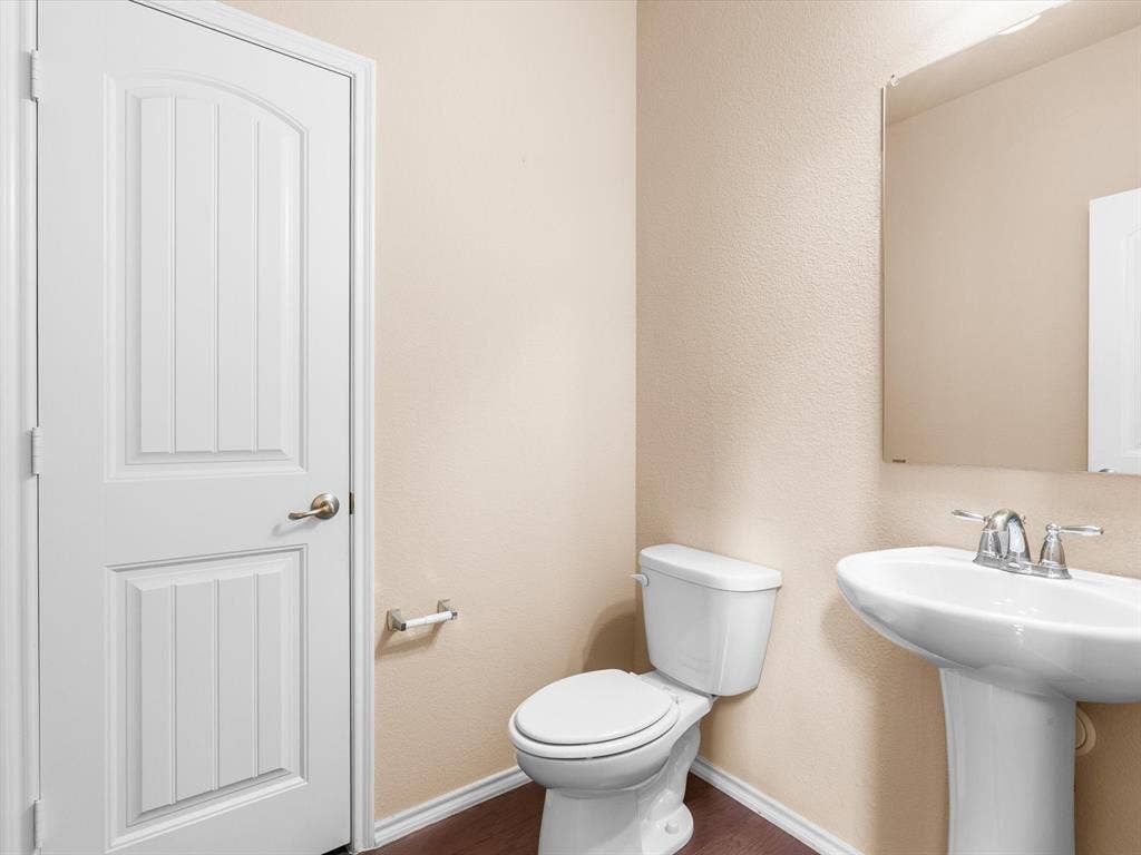 Half- bath. Pedestal sink with polished chrome faucet, wood-finish flooring, and white paneled door