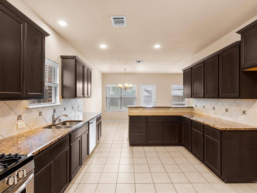 Kitchen featuring dark-finish cabinetry, stone-surface countertops, tile backsplash with decorative accents, recessed lighting, and tile flooring