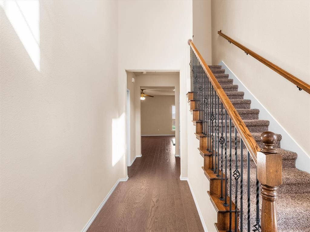 Entryway featuring high ceilings, wood-finish flooring, and a staircase with stained wood handrails, ornamental metal balusters, and carpeted treads