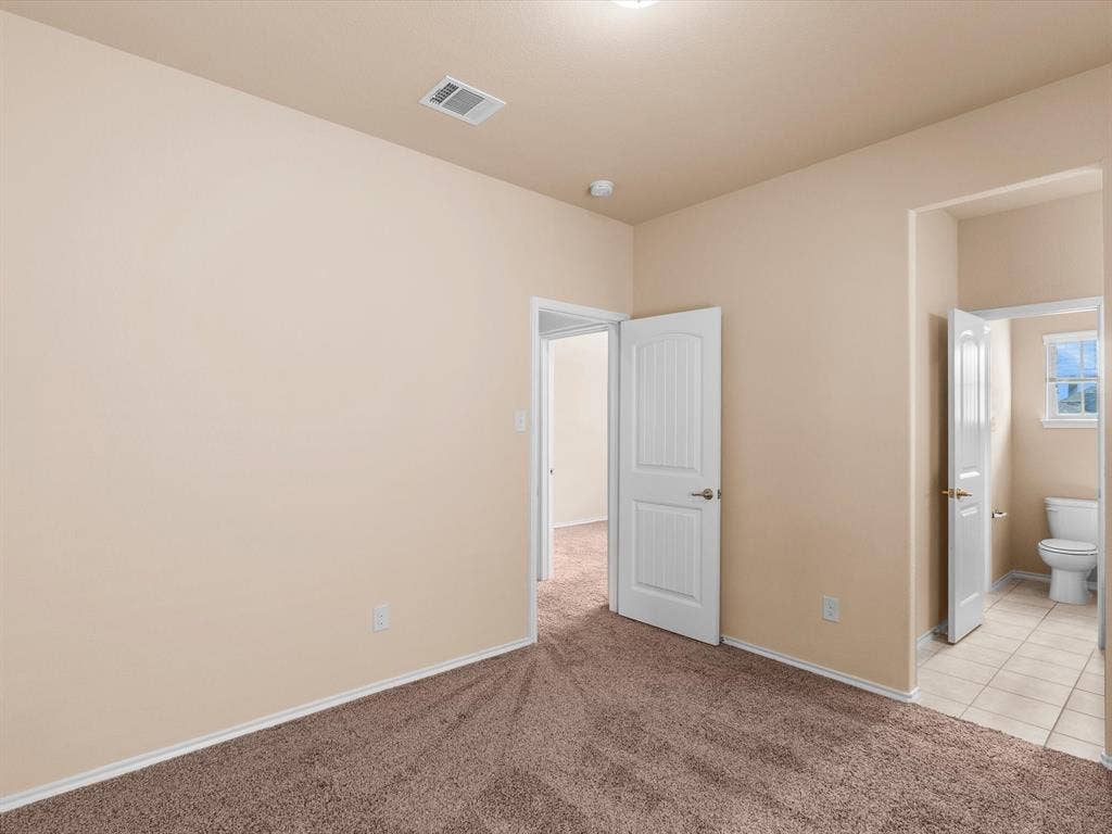 Room with neutral-toned walls, plush carpeting, multi-panel interior doors, and tile flooring within the secondary space