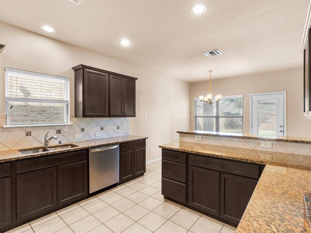 Kitchen featuring dark-finish cabinetry, stone-surface countertops, tile backsplash, stainless steel dishwasher, and ceramic tile flooring