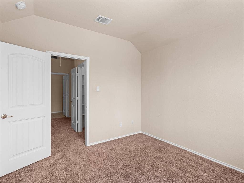 Neutral wall color, wall-to-wall carpeting, vaulted ceilings, and a paneled interior door with satin nickel hardware