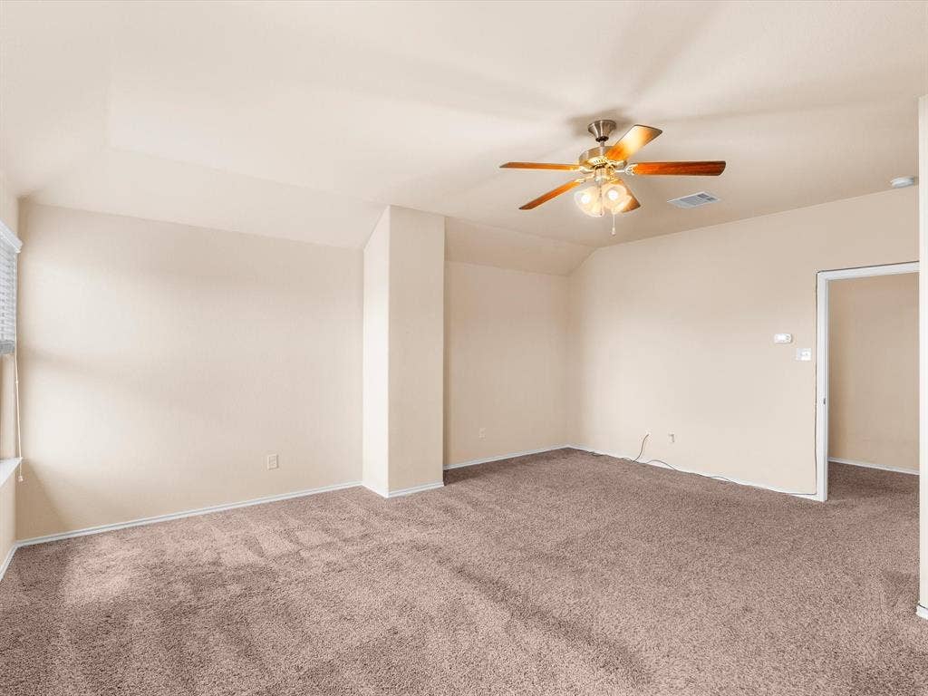 Room featuring neutral wall-to-wall carpeting, vaulted ceilings, and a central ceiling fan with integrated lighting